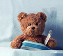 Teddy bear sitting in bed with a thermometer under its arm