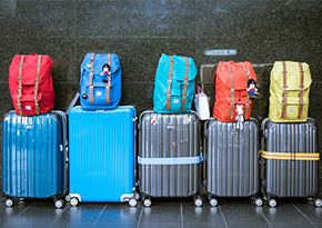 five coloured suitcases on wheels with a backpack stacked on top of each one 