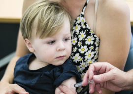 Toddler sitting in mum's lap recieving vaccination