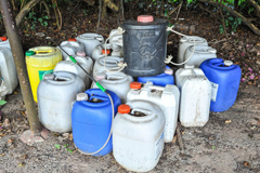 A collection of coloured containers of household chemicals and poisons kept insecurely in a garden 