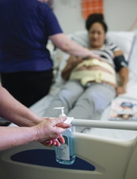 Health care worker using alcohol-based hand rub before treating a patient in hospital