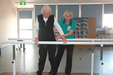 A health care professional helping person leaning on a bar during therapy