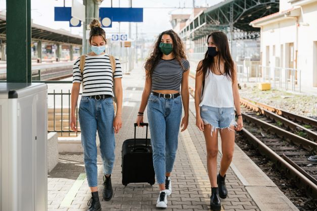 Three women wearing facemasks standing on train platform