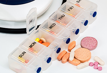 Pills of a variety of shapes and sizes in and around a weekly pill container